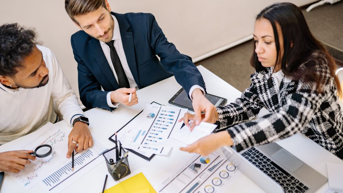 A diverse team of professionals in business attire reviewing charts and financial reports together at a desk.
